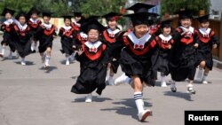 China -- Children in gowns and mortarboards run with smiles during their kindergarten graduation ceremony in a kindergarten in Handan, Hebei province, June 20, 2017