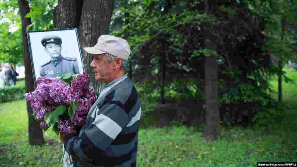 Соғысқа қатысқан майдангер суреті мен гүл ұстап келе жатқан ер адам. Алматыдағы &laquo;Мәңгілік полк&raquo; шеруі.