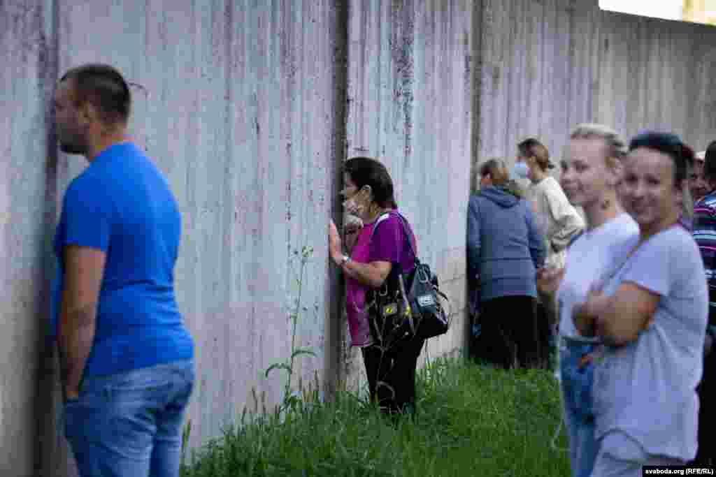 Людзі, якія празь вялікую чаргу не змаглі трапіць на перадвыбарчы пікет кандыдаткі ў прэзыдэнты Сьвятланы Ціханоўскай у Слоніме, назіраюць за яе выступам праз шчыліны ў агароджы футбольнага стадыёну. 1 жніўня